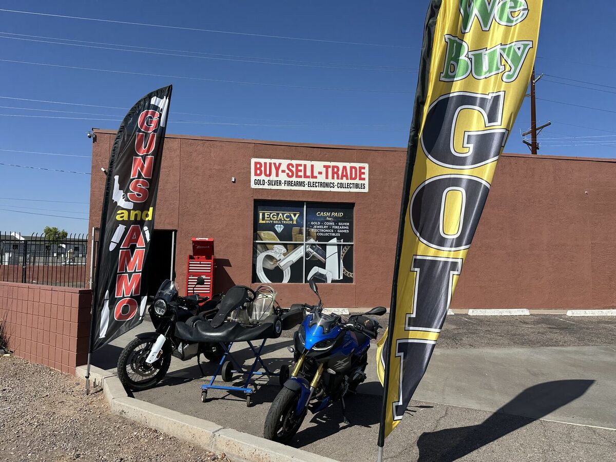 Legacy storefront at 240 N Gilbert Rd in Mesa with We Buy Gold and Guns and Ammo flags out front
